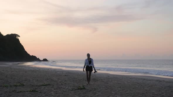Young smiling woman walking barefoot in the sand towards camera at sunset on Nacpan Beach, Palawan,