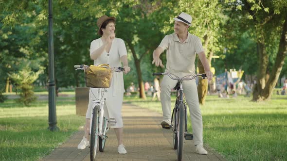 Wide Shot of Cheerful Mid-adult Man and Woman Giving High Five As Sitting on Bicycles in Sunlight