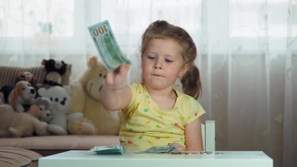Blonde four-year-old girl is counting American banknotes, cash, sitting at the table at home.
