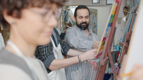 Young Woman Drawing Picture While Helpful Teacher Helping Man with Portrait in Art School