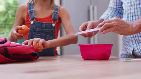 Midsection of caucasian grandfather in kitchen preparing packed lunch with granddaughter