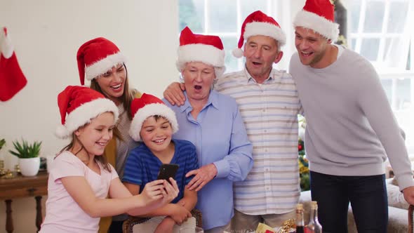 Caucasian family wearing santa hats using smartphone together in the living room at home