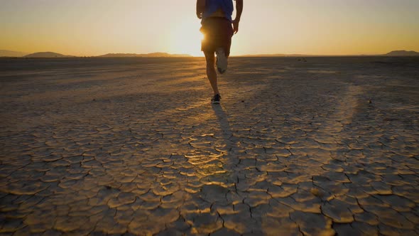 Athletic man working out with battle ropes on a dry lake at sunset