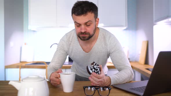 Bearded Man Having Breakfast in the Kitchen and Using a Laptop