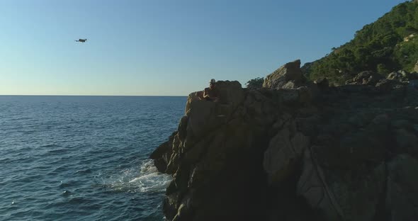 Traveler with flying drone on rocky sea coast