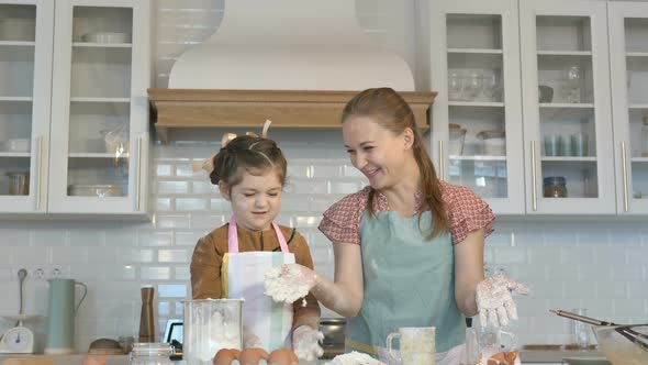 Cheerful Girl and Mommy Throw Flour Making Dough in Kitchen