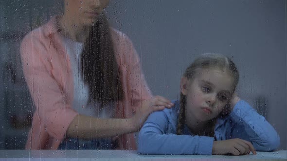 Mother Supporting Little Girl Behind Rainy Window