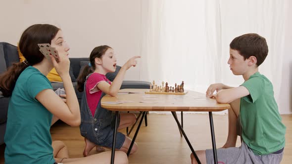 Three kids playing a card game in the living room, shouting and arguing