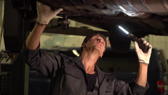 Caucasian car mechanic looking with light while preparing adjusting tension in vehicle suspension