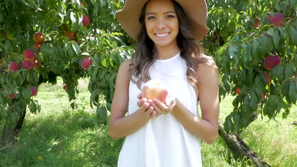 Young woman excitedly holds out a large, ripe peach she has picked.