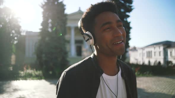 Portrait of Young Stylish Hipster Black Man in White Headphones and Sun Glasses Dancing Outdoor in