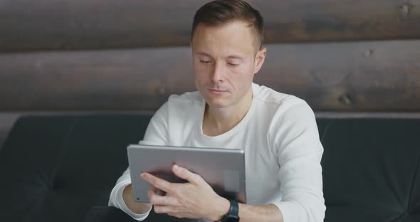 Young Thoughtful Man Uses Tablet While Sitting on the Couch