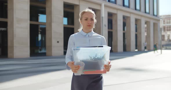 Upset Businesswoman Walking Outdoors with Box of Stuff Leaving Business Center