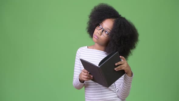 Young Cute African Girl with Afro Hair Studying Against Green Background