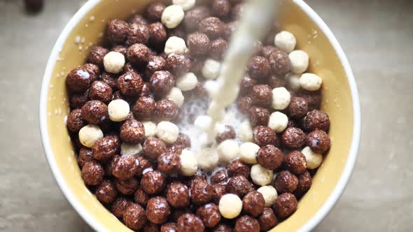 Fresh Milk is Poured Into a Bowl Filled with Chocolate Grain Balls