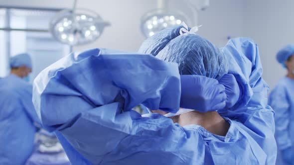 Mixed race female surgeon putting on protective clothes standing in operating theatre