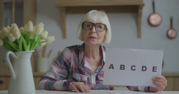 Senior Teacher in Glasses Showing Sheet of Paper with Alphabet Letters Looking at Camera