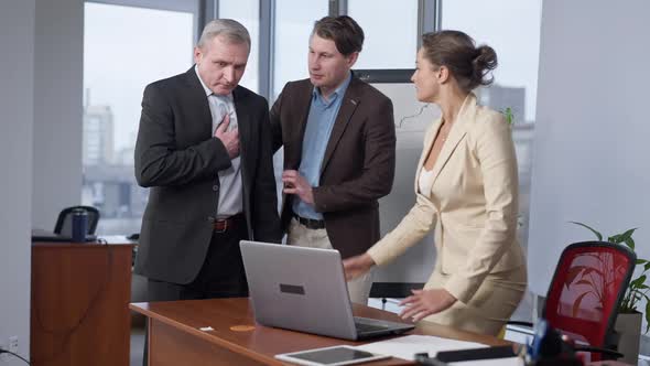 Caucasian Man and Woman Supporting Senior Colleague Having Symptoms of Heart Attack