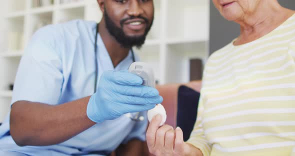 Video of midsection of african american male doctor checking glucose level to caucasian senior woman