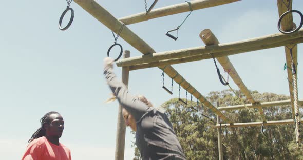 Fit caucasian woman falling from bars at obstacle course helped by african american male colleague