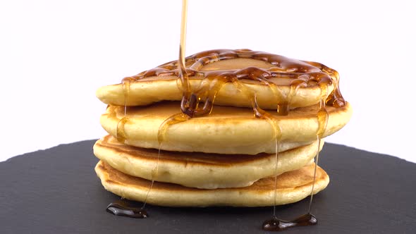 American pancakes with maple syrup on a white background. Pancake lies on a black slate round stone.