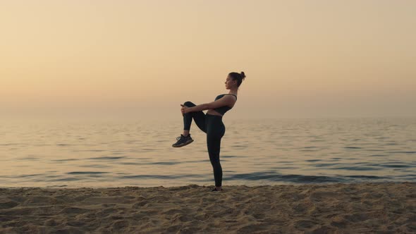 Sporty Girl Holding Knee Stretching Legs on Beach