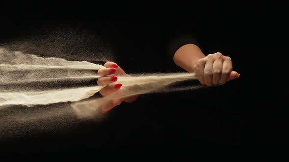 Stream of Dry Sand Pours Into Palm of Woman and is Spilling Through Her Fingers on Black Background