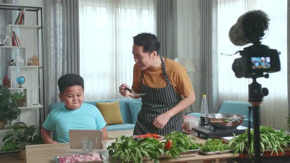 Asian Father And Son Record Video With Camera While Cooking At Home, Food Tasting And Thumbs Up