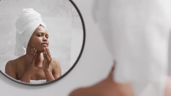 Happy african american woman apply cream on face in bathroom