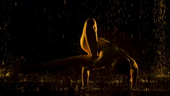 Slender Woman Wet From the Rain Performs a Difficult Handstand in a Dark Studio. The Sexy Body Is