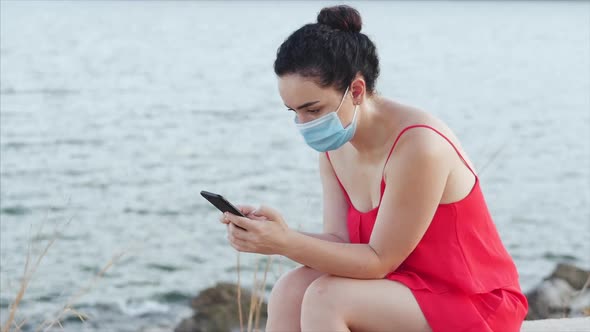 Young Woman in a Mask From the Coronavirus Epidemic Sits on the Shore Near the Sea in Solitude,types