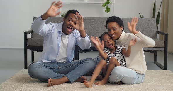 Afro American Family Three People Daughter Mom Dad Waving at Camera While Sitting on Floor of House