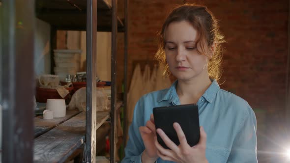 Slow Motion of Serious Girl Using Tablet in Pottery Workshop Looking at Ceramics