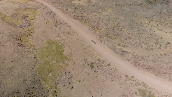 aerial shot following two mountain bikers climbing up a gravel road mountain pass