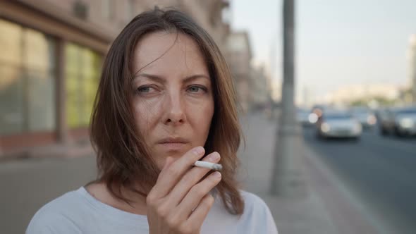 Adult Woman is Smoking Cigarette Standing on City Street at Summer Day Viewing Car Traffic