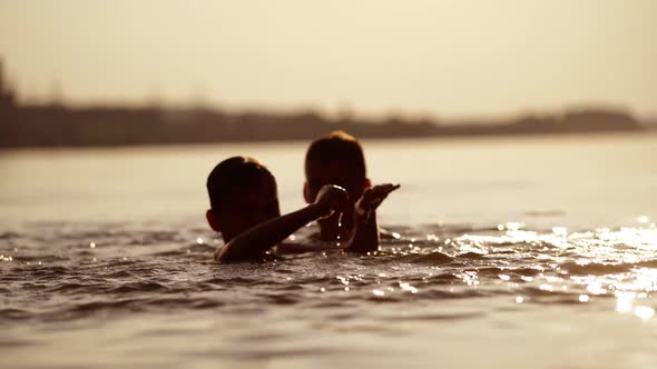 Silhouette of two boys swimming and playing with water at sunset.