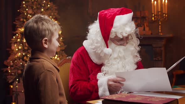 Santa Claus and little boy. Cheerful Santa is working at the table. Christmas concept.