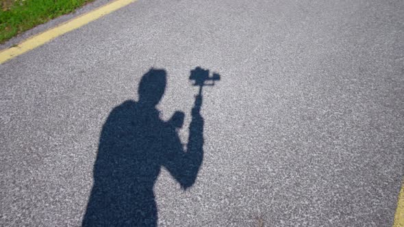 Operator Shadow Moves Filming Asphalt Road Near Grass