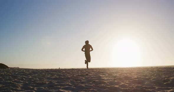 African american man running on beach, exercising outdoors in beach in the evening