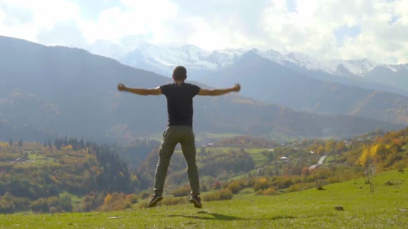 man jumps and claps his hands against background of autumn mountains.