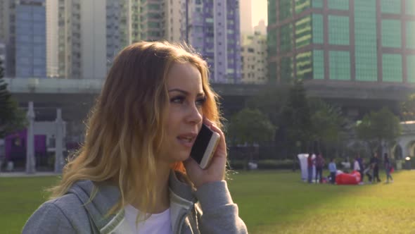 Woman Talks on Cellphone on Fresh Green Meadow in City Park