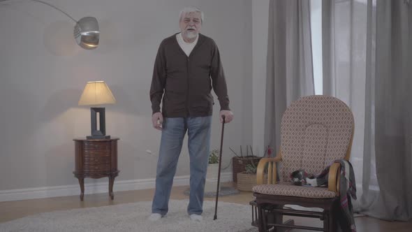 Portrait of Old Caucasian Man with Walking Cane Gesturing As Listening To Music at Home. Wide Shot