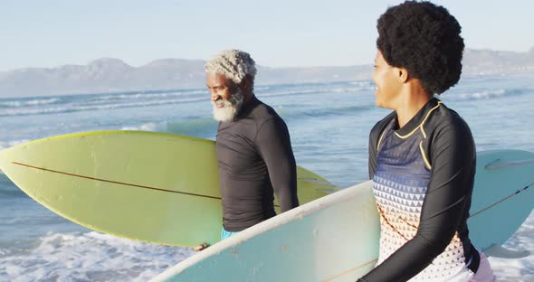 Happy african american couple walking with surfboards on sunny beach