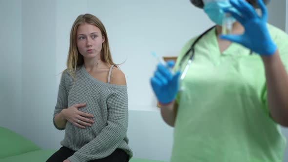 Portrait of Young Pregnant Woman Touching Belly Sitting in Vaccination Center As Doctor Filling in