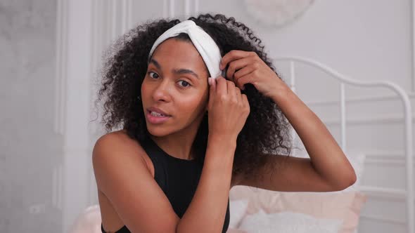 Dark Skin Woman Putting on Headband and Smiling at Camera in Bright Room