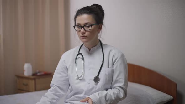 Front View Portrait of Young Intelligent Doctor Putting on Eyeglasses Looking at Camera Writing with