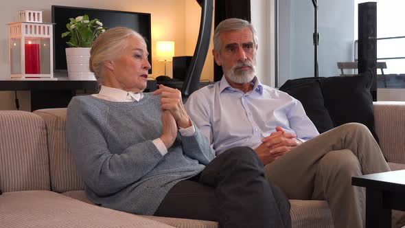 An Elderly Couple Sits on A Couch in An Apartment and Talks