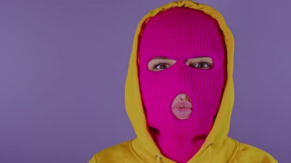 Unrecognizable Woman in Pink Balaclava Sending Blowing Kisses on Purple Background