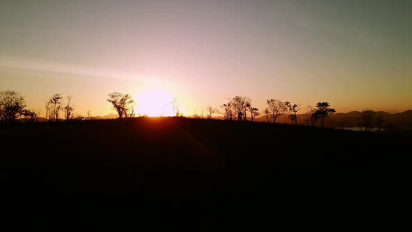 Aerial drone shot of dramatic sunset, flying above silhouette of trees and hills. Sun sets amid isla