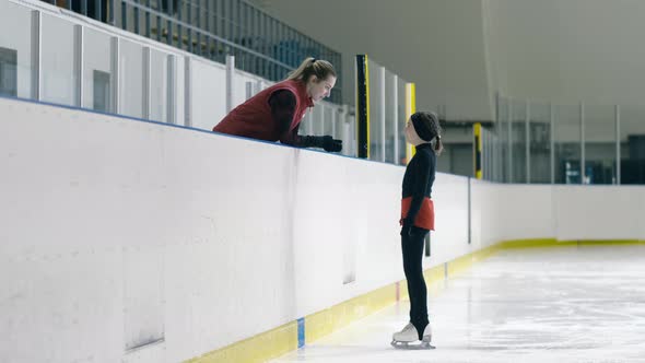 Young figure skater on ice listening to her trainer's comment